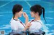 Two young women in a swimming pool with their hands together.