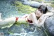 A woman in a red bikini laying on a rock in the water.