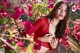 A woman in a red dress posing in front of pink flowers.