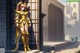 A woman in a gold outfit standing in front of a building.